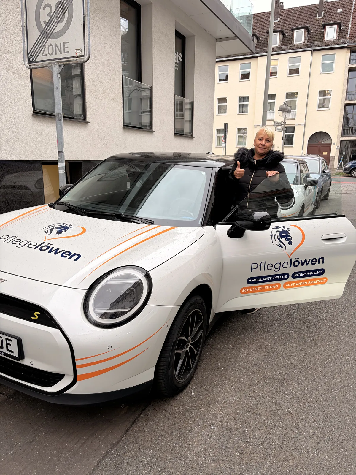Pflegelöwen-Mitarbeiterin mit Daumen hoch am E-Auto – werde Teil des Rudels